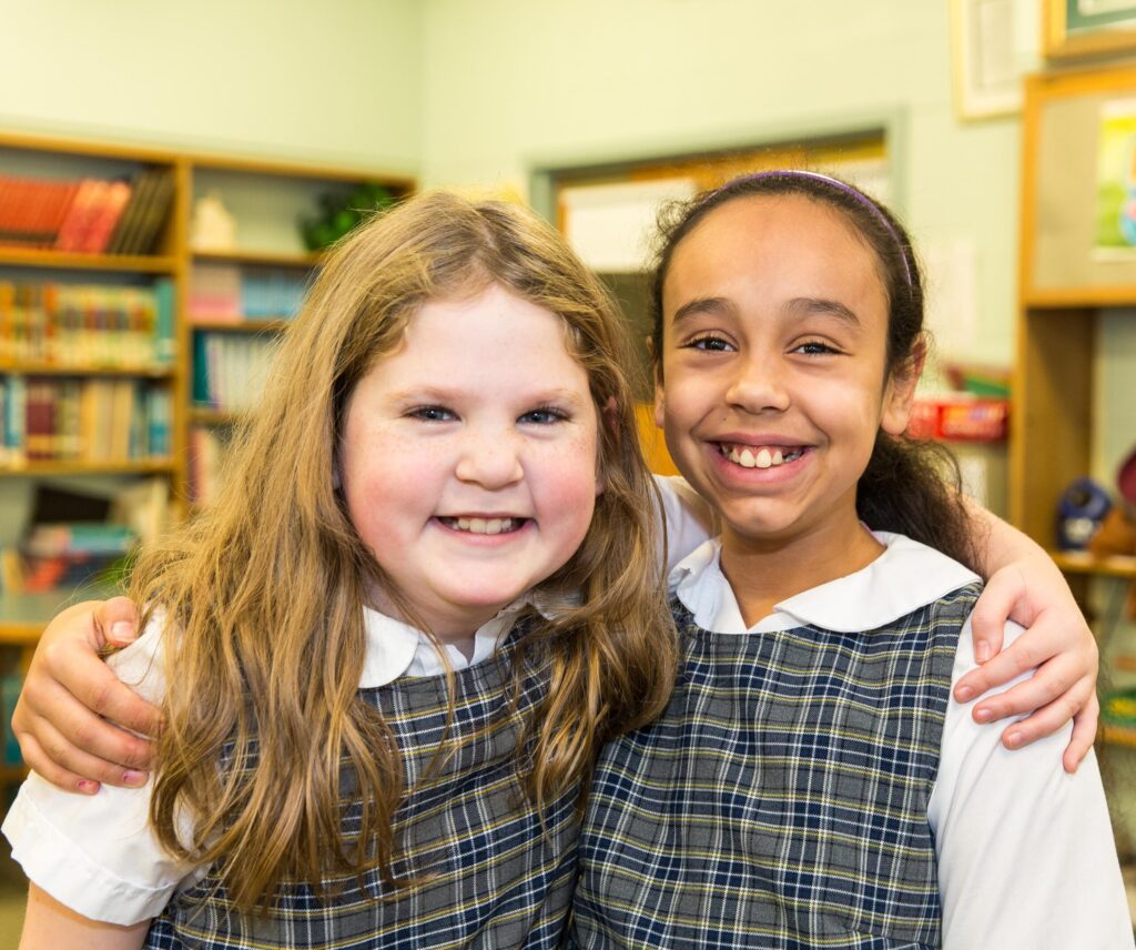 Two students in school uniforms smiling together in a classroom