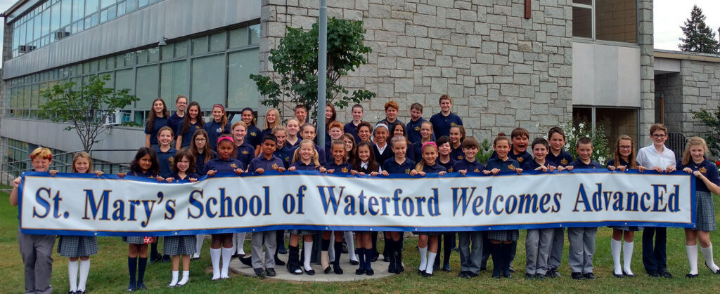 Students and staff holding a banner that reads ‘St. Mary’s School of Waterford Welcomes AdvancED’ outside the school building