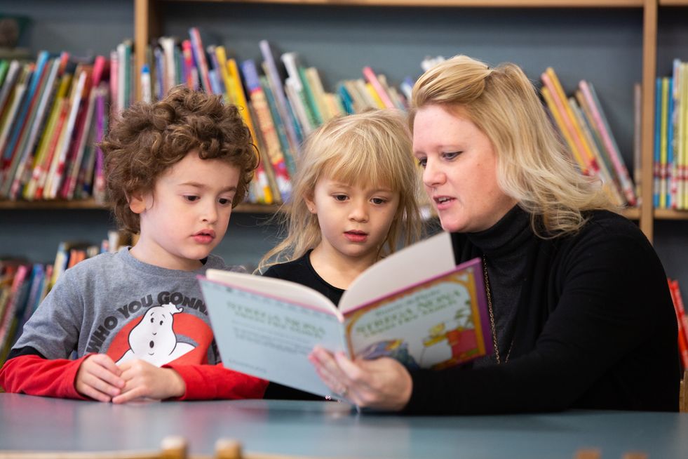 Teacher reading a book with two young students in a classroom